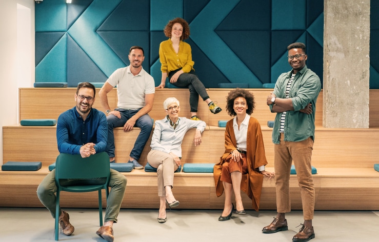 Group of multi ethnic creative people in smart casual wear looking at camera and smiling in creative office workplace. Coworker teamwork concept.
